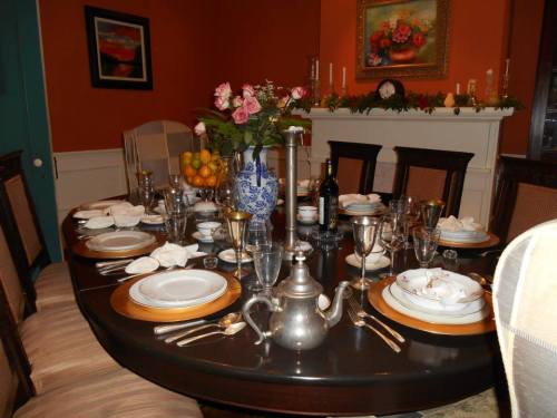 A beautifully set dining table with elegant tableware, flowers, and a decorative vase against a warm orange wall.