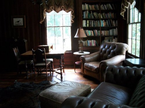 Cozy room with a bookshelf, a table and chairs, a lamp, and comfortable seating by a large window.