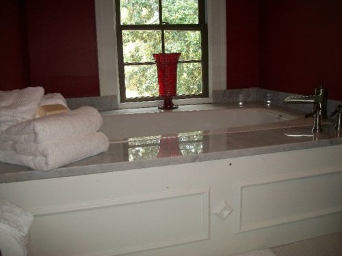 A luxurious bathroom featuring a marble tub, stacked white towels, and a red vase by a window.