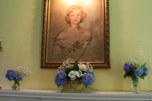 A portrait of a woman hangs above a mantel adorned with floral arrangements in blue and white vases.
