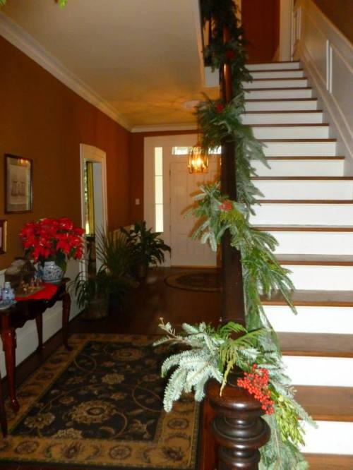 A warmly decorated hallway with a staircase, greenery garland, and festive plants, creating a welcoming atmosphere.