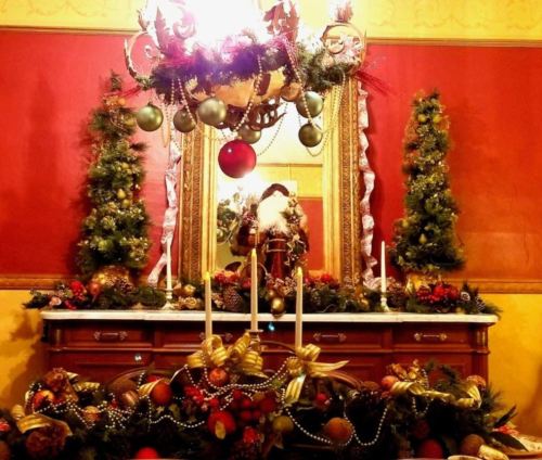 A festive holiday display featuring a decorated mirror, Santa figure, and lush greenery on a wooden dresser.
