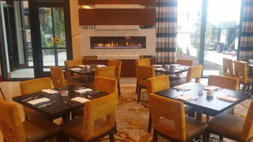 A modern restaurant interior featuring tables with yellow chairs and a fireplace in the background.