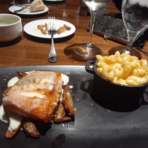 A plate featuring salmon with creamy sauce, roasted potatoes, and a side of macaroni and cheese in a small dish.