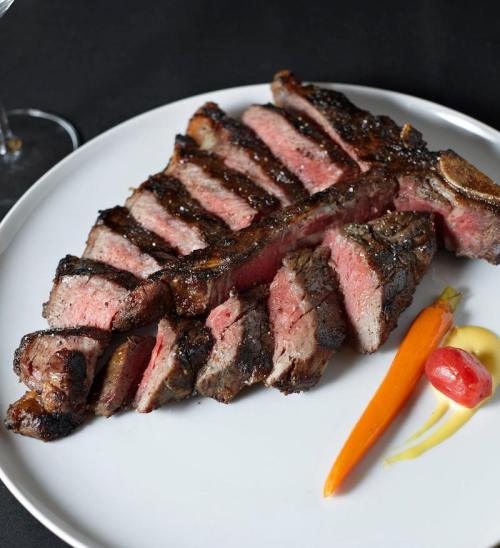 A perfectly cooked steak, sliced and served on a white plate with a small carrot and a dollop of sauce.