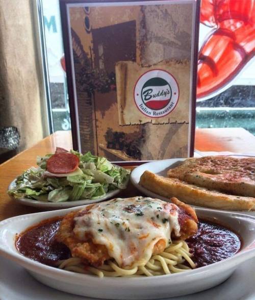 A plate of chicken parmesan on spaghetti with marinara, a side salad, and breadsticks, next to an Italian restaurant menu.