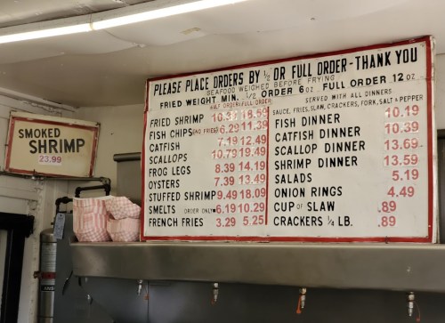 Menu board displaying seafood prices and order options, including shrimp, catfish, scallops, and sides.