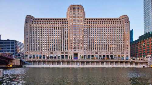 Historic building along a river, featuring a symmetrical facade with numerous windows and a prominent rooftop.