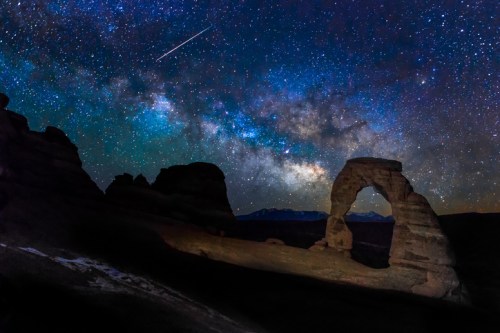 A stunning night sky filled with stars and the Milky Way, featuring a rock arch silhouette in the foreground.