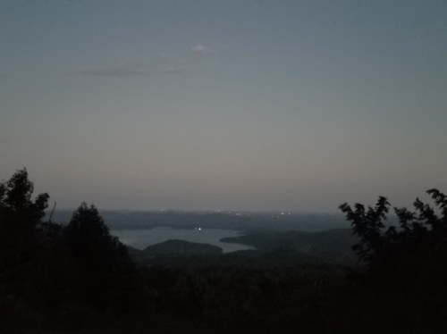 A serene twilight landscape featuring a lake surrounded by hills and distant lights in the horizon.