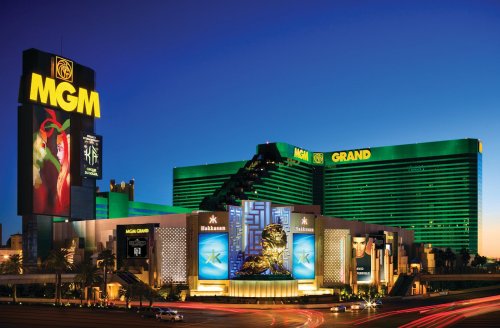 MGM Grand hotel in Las Vegas at dusk, featuring bright green lights and a large lion statue at the entrance.