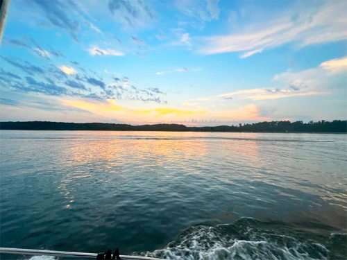 A serene sunset over calm waters, with colorful clouds reflecting on the surface and a distant shoreline.