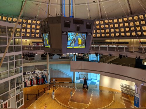 A spacious basketball hall of fame with a large scoreboard and a court, featuring displays and a dunk area.