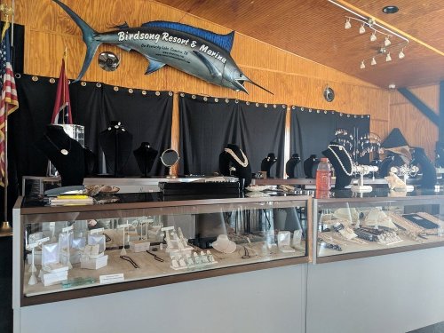 Display of jewelry in a shop with various necklaces and rings, under a sign for Birdsong Resort & Marina.