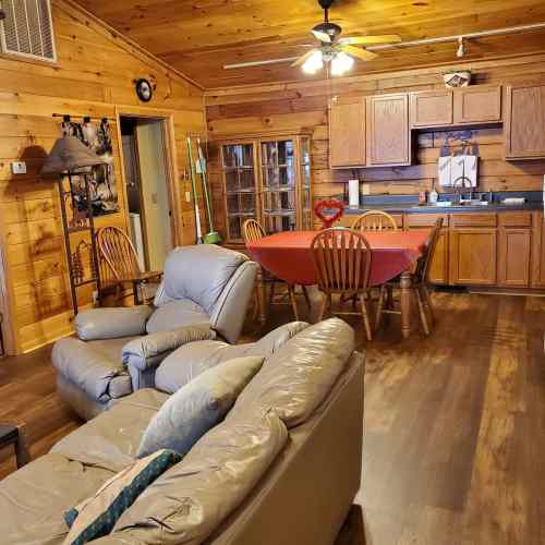 Cozy wooden interior with a living area, dining table, and kitchen, featuring warm lighting and rustic decor.
