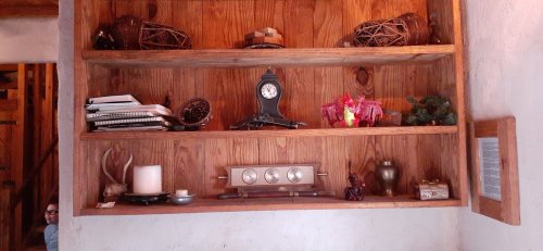 A wooden shelf displaying various decorative items, including a clock, books, and small sculptures.