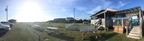 A panoramic view of an outdoor dining area with picnic tables, a building, and a clear blue sky.