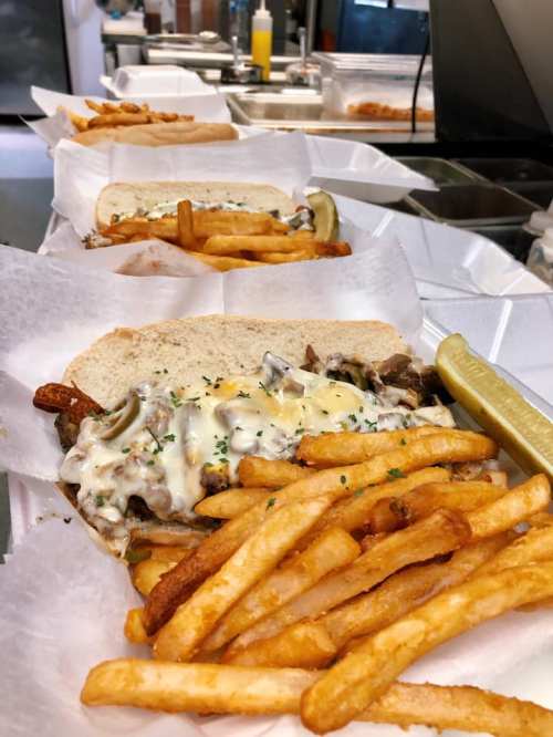Three sandwiches topped with melted cheese and sautéed onions, served with crispy fries and a pickle on the side.