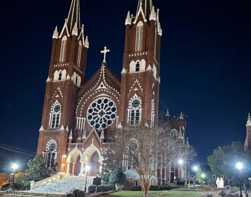 A large brick church with twin spires and a rose window, illuminated at night against a dark sky.