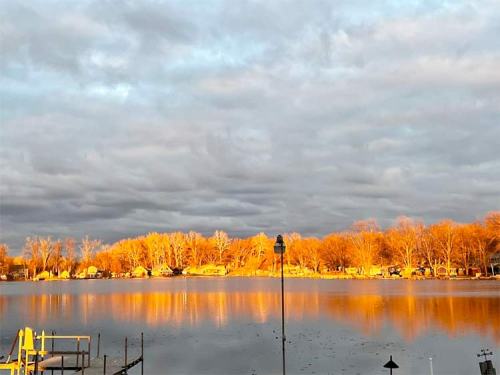 A serene lake at sunset, reflecting golden light on the water and surrounded by trees and clouds.