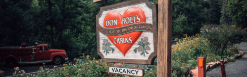 Sign for Don Hoel's Cabins with a heart design, surrounded by greenery and flowers, indicating "Vacancy."