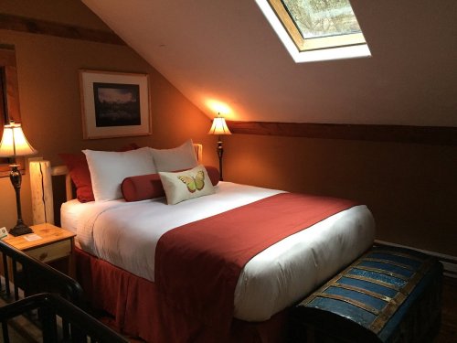Cozy bedroom with a sloped ceiling, featuring a bed with red accents, a skylight, and warm lighting.