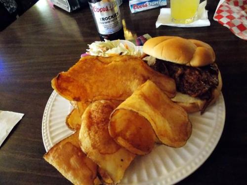 A plate with a pulled pork sandwich, coleslaw, and a generous serving of crispy potato chips.