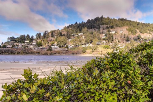 A scenic view of a coastal town nestled among green hills, with a sandy beach in the foreground and blue sky above.