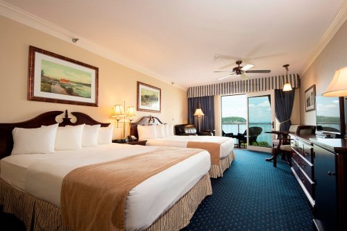 A hotel room featuring two beds, a balcony with a view, and warm lighting, creating a cozy atmosphere.