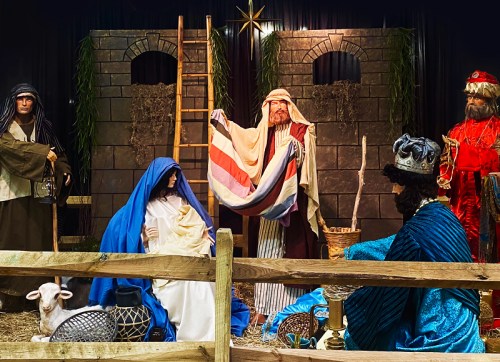 Nativity scene with figures of Mary, Joseph, and the Three Wise Men, set against a rustic backdrop with a sheep.