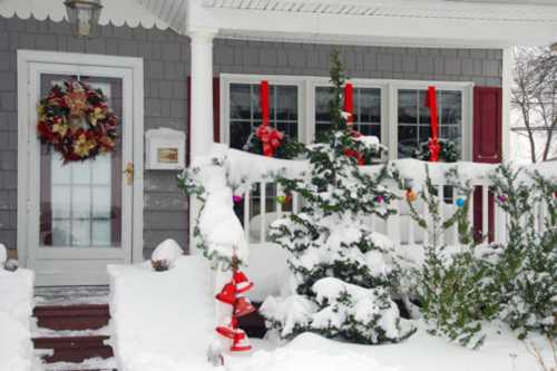 A snowy porch decorated with a wreath, red ribbons, and colorful ornaments on a winter day.