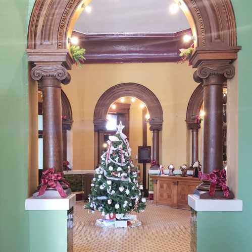 A festive interior with ornate columns, a decorated Christmas tree, and holiday decorations in a warm, inviting space.