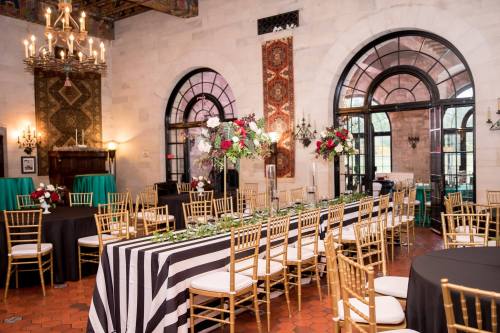 Elegant dining room set for an event, featuring striped tablecloths, floral centerpieces, and gold chairs.