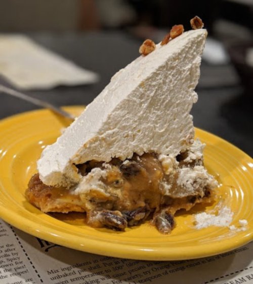 A slice of dessert with a thick layer of whipped cream on top, resting on a yellow plate.