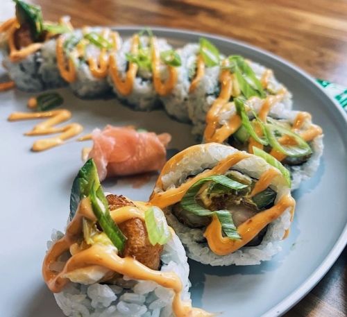 A plate of sushi rolls topped with green onions and a drizzle of sauce, accompanied by pickled ginger.