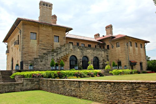 Historic stone mansion with a tiled roof, multiple chimneys, and landscaped gardens.