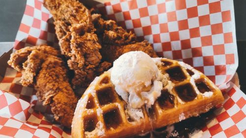 A plate of crispy fried chicken served with a golden waffle topped with butter and syrup, in a checkered basket.
