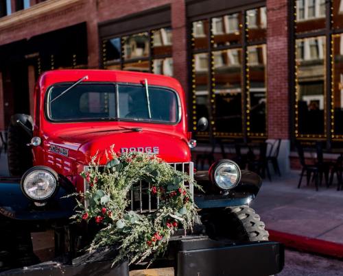A vintage red Dodge truck adorned with a festive wreath, parked in front of a building with reflective windows.