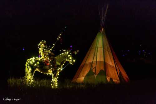 A illuminated figure on a horse, adorned with lights, stands beside a glowing teepee in a dark setting.