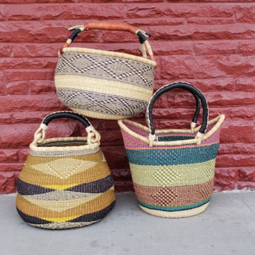 Three colorful woven baskets with various patterns, resting against a textured red wall.
