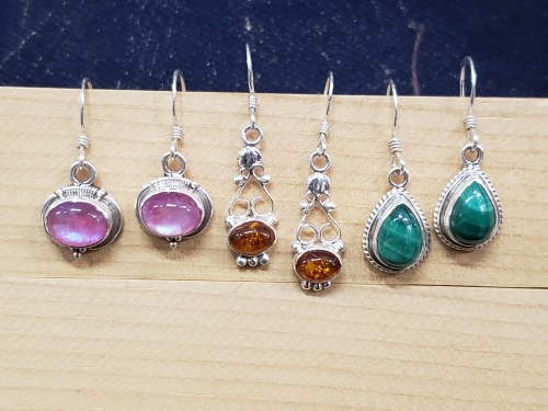 A collection of six pairs of earrings featuring various gemstones in silver settings, displayed on a wooden surface.