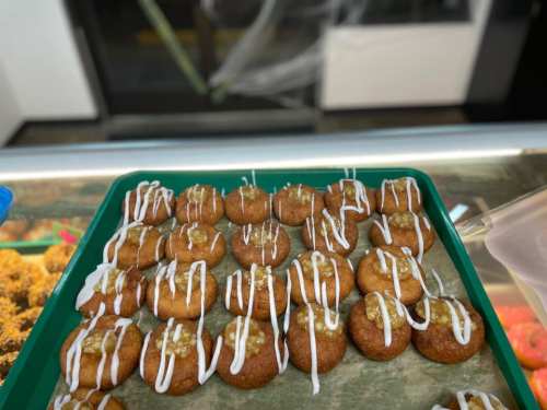 A tray of small, round pastries drizzled with white icing, arranged neatly on a green tray.