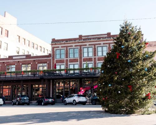 A large Christmas tree decorated with ornaments stands in front of a brick building adorned with festive decorations.