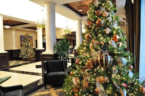 A beautifully decorated Christmas tree with ornaments and lights, set in an elegant lobby with another tree in the background.