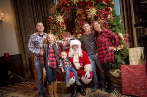 A family poses with Santa Claus in front of a festive Christmas tree and decorations.