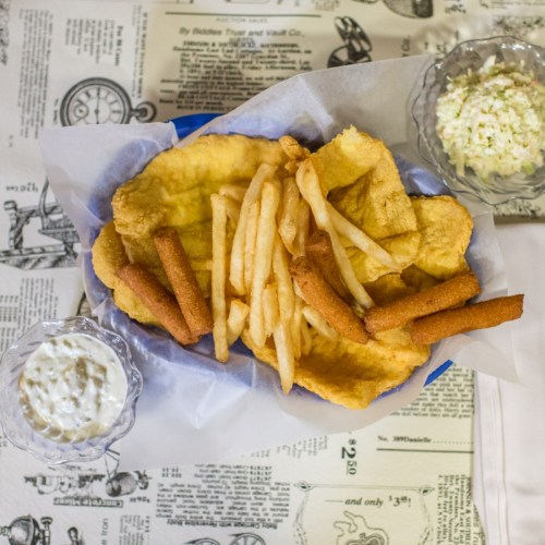 A plate of fried fish, golden fries, and hushpuppies, served with a side of tartar sauce and coleslaw.