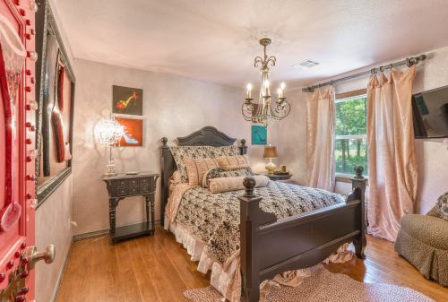 Cozy bedroom featuring a black bed, elegant chandelier, and soft curtains, with warm wooden floors and decorative accents.