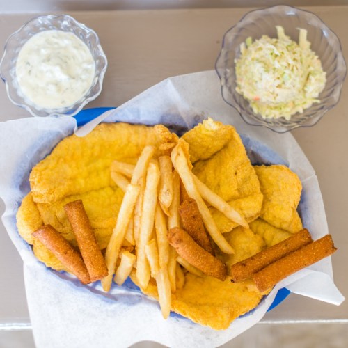 A plate of golden fried fish fillets, French fries, hushpuppies, and a side of coleslaw with dipping sauce.