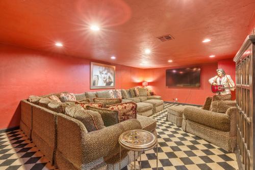 Cozy basement lounge with red walls, patterned sofas, a large TV, and checkered flooring.