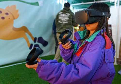 A child wearing a VR headset holds controllers, immersed in a virtual reality experience at an event.